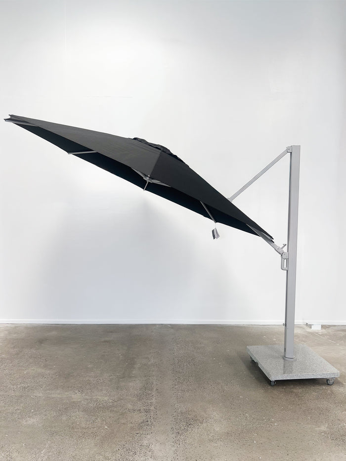 Black patio umbrella on a stand against a white wall