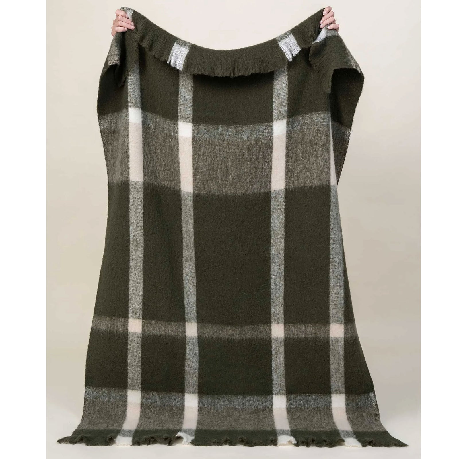 Plaid blanket with green, and white pattern held up against a plain background