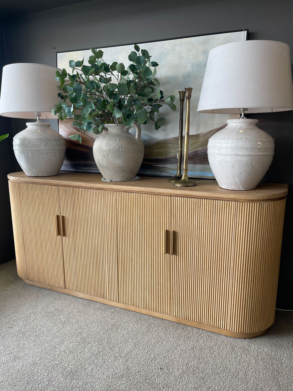 Wooden sideboard with decorative items including lamps and a plant against a dark wall.
