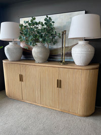 Wooden sideboard with decorative items including lamps and a plant against a dark wall.