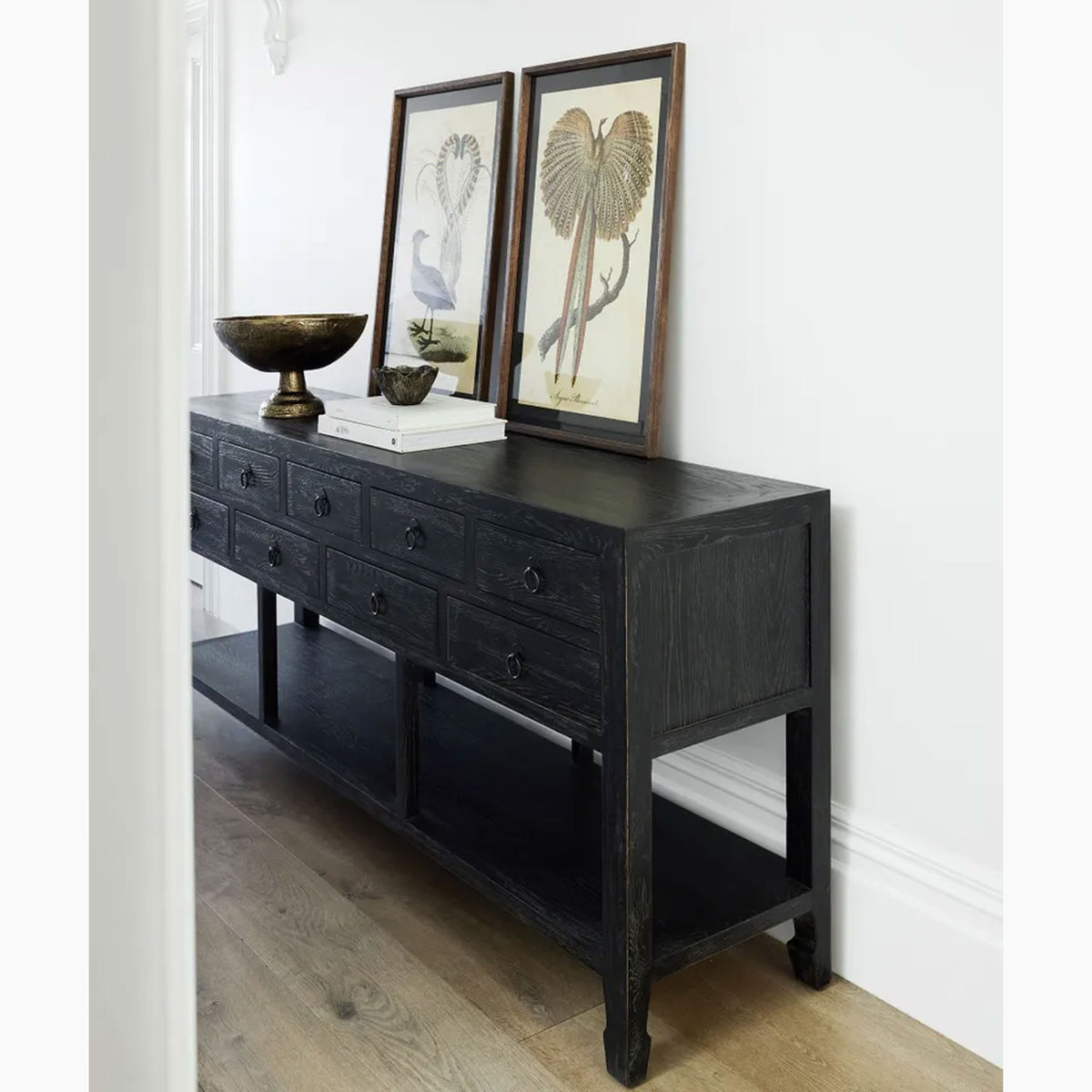 Black console table with framed artwork and decorative items against a white wall.