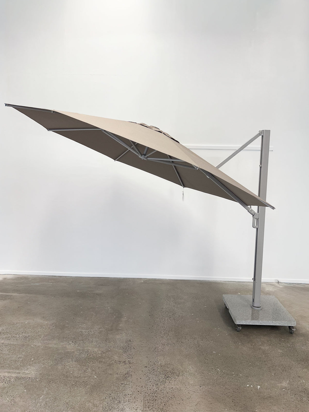 Beige outdoor umbrella on a stand against a white wall