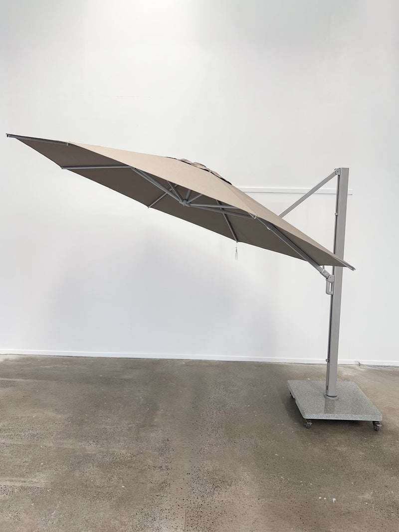 Beige outdoor umbrella on a stand against a white wall
