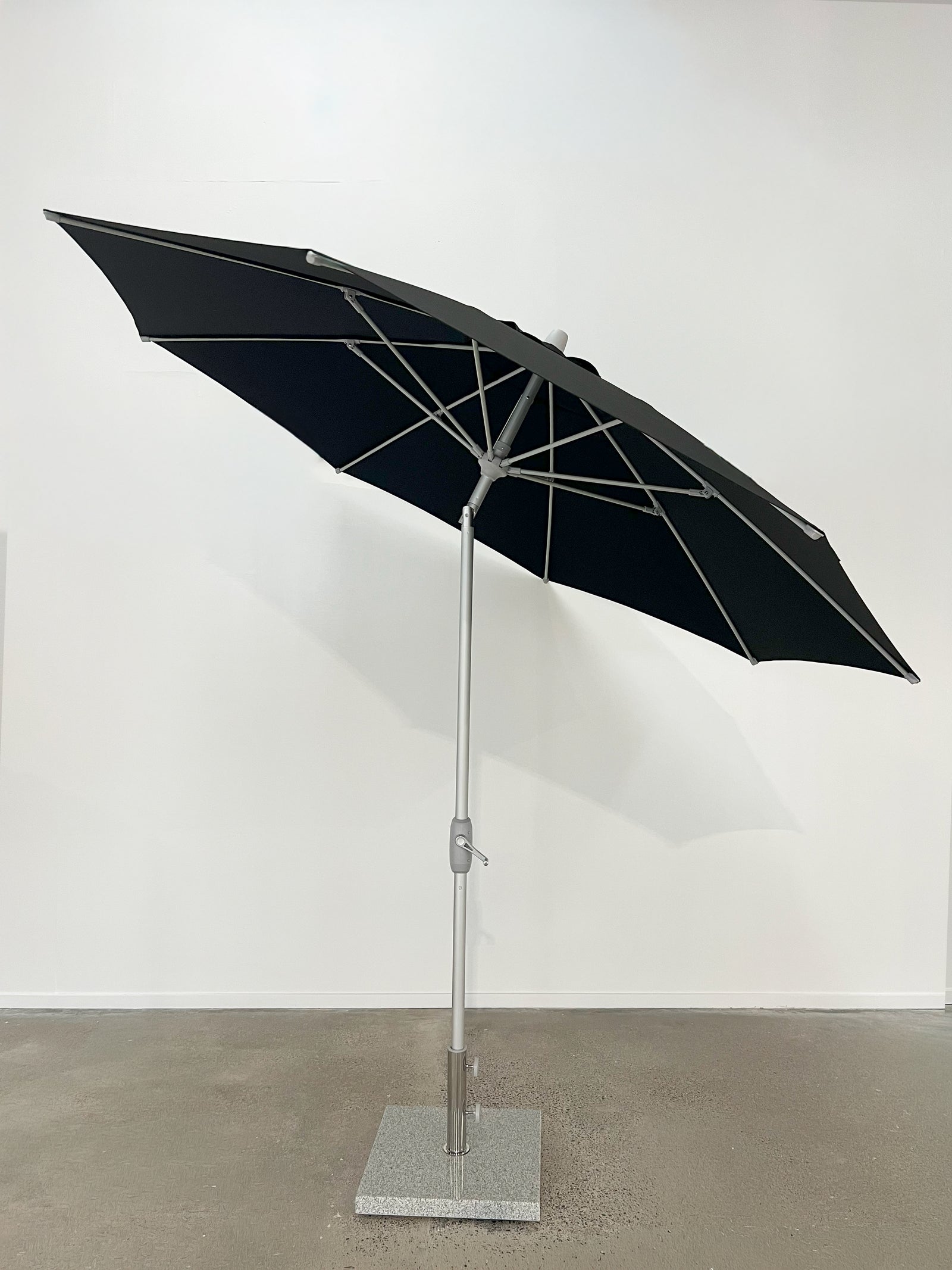 Black patio umbrella on a stand against a white wall