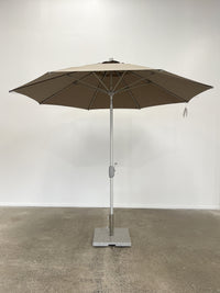 Brown patio umbrella with a stand on a concrete floor against a white wall