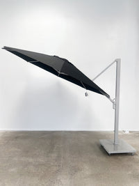 Black patio umbrella on a stand against a white wall